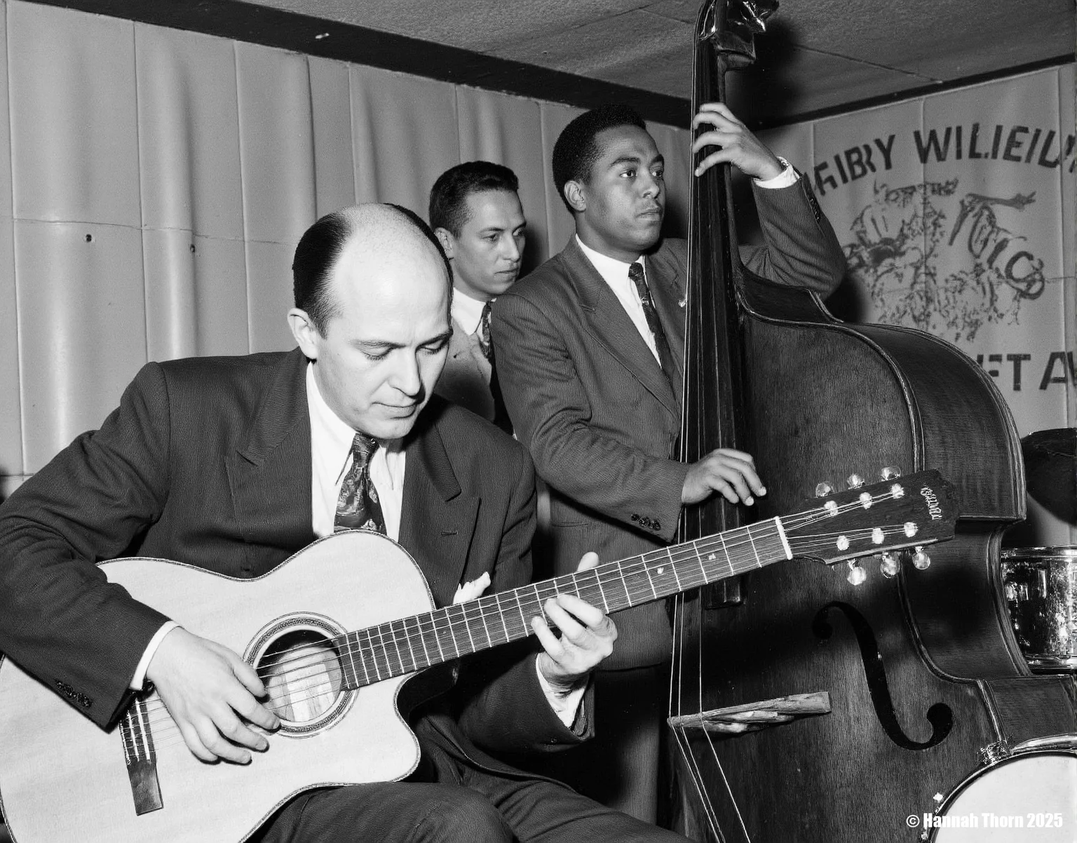 The picture is a black and white photograph of a jazz ensemble in what appears to be a club or bar setting.    The image shows three musicians prominently featured.  In the foreground, a man with a bald head is seated, playing a classical guitar. He is wearing a dark suit and tie. To his right, a man plays an upright double bass; he is African American, wearing a suit and tie, and  is engrossed in playing his instrument. Behind the guitarist, partially obscured, is a third musician, a fair-skinned man with short hair, also in a suit and tie. He's likely a drummer, as a snare drum is visible behind him.  The background suggests a simple, somewhat dimly lit venue. There is visible wood paneling on the wall and a glimpse of a tiled ceiling. Part of a wall-mounted advertisement or artwork is visible in the upper right corner.  The style of the photograph is consistent with mid-20th-century photojournalism or documentary photography. The black and white palette, candid composition, and focus on the musicians in an informal setting, all contribute to this stylistic identification.  The image has a slightly grainy texture characteristic of older photographic processes. The lighting is somewhat subdued, likely typical of a dimly lit club at night, casting a certain moodiness onto the scene. The overall feel is one of realism and authenticity, capturing a moment in time. <lora:_Flux\Vintage_Jazz-Club.safetensors:1.0:1.0>