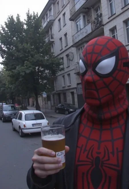 d1g1cam, Spiderman with mask drinks beer, in 2000s early, Dull and overcast lighting, his face partially shadowed, amateur photo, low-lit, Low-resolution photo, shot on a mobile phone, evening, noticeable noise in dark areas, he is standing on the street near soviet-era storey buildings, trees, parked cars near, outdoors