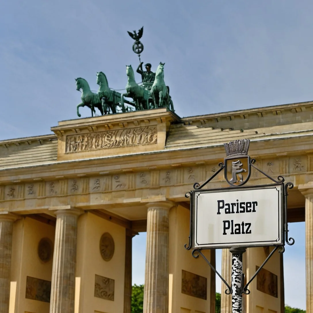 Berlin, Brandenburg Gate, historical architecture, Pariser Platz,
brandenburg gate in berlin, six tall columns, 6 tall pillars, neoclassical columns, quadriga on top, quadriga statue on top,
real photo, realistic, photorealistic, outdoor,
cobblestone ground, cobblestone plaza, Pariser Platz.
pariser platz, ornate street sign reading "pariser platz", sign with text "pariser platz", pariser platz sign,
metal sign with crown and berlin crest, urban detail, berlin