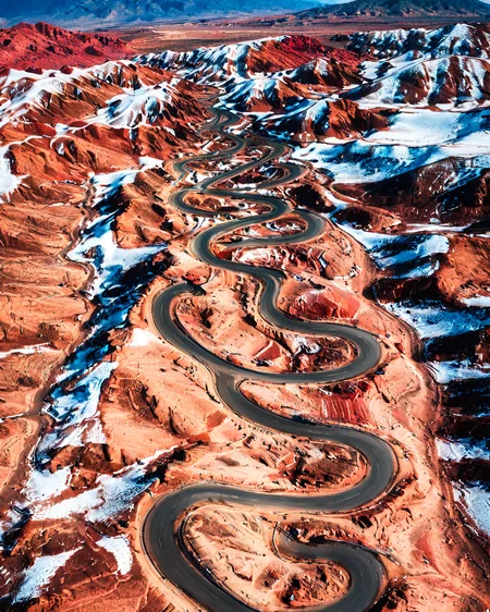 vertical perspective aerial photography, desert_road, red_rock_terrain, undulating_hills, clear_skies, travel car on road, <lora:sky:0.8>