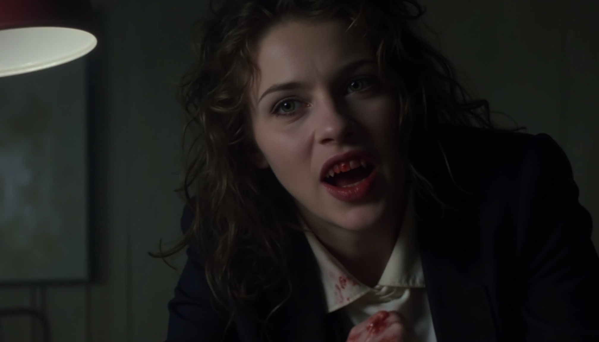 cinematic close-up shot of a young vampire business woman with fangs sitting on a desk, looking intensely at the viewer, very pale skin, mouth open showing fangs, blood around mouth, blood on white blouse, dark suit, messy hair hanging over face, lit from one side by a desk lamp with cold light, shadow on the other side, strong contrast between pale skin and blood, analogue film, IMAX, photorealistic, very detailed <lora:iwtv_flux_1_0:1>