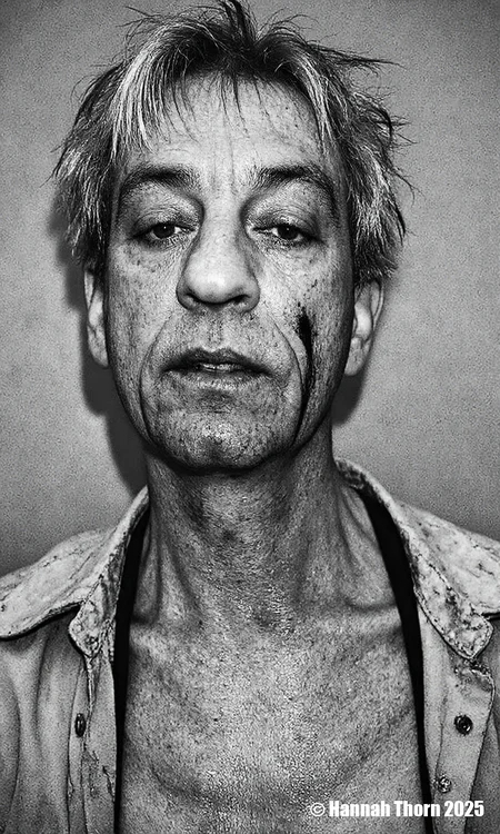 A black and white portrait of a middle-aged man with short, messy hair and a serious expression. he appears to be in his late 60s or early 70s, with light skin and a slightly wrinkled face. his eyes are closed, and he is looking directly at the camera. his hair is messy and unkempt, with some strands falling down his back. he has a black shirt draped over his shoulders, and there are scars on his face and neck, suggesting he has been involved in a serious or intense situation. the background is a plain, textured wall, and the lighting is dramatic, casting shadows on the man's face and upper body. the overall mood of the image is somber and contemplative.<lora:_Flux\Anders_Petersen.safetensors:1.0:1.0>