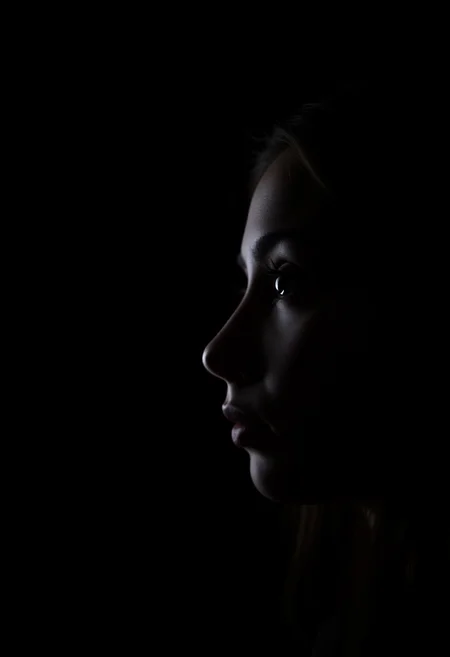 A realistic side profile of a girl against a black background, captured in low lighting, highlighting her face in a simple, moody portrait.