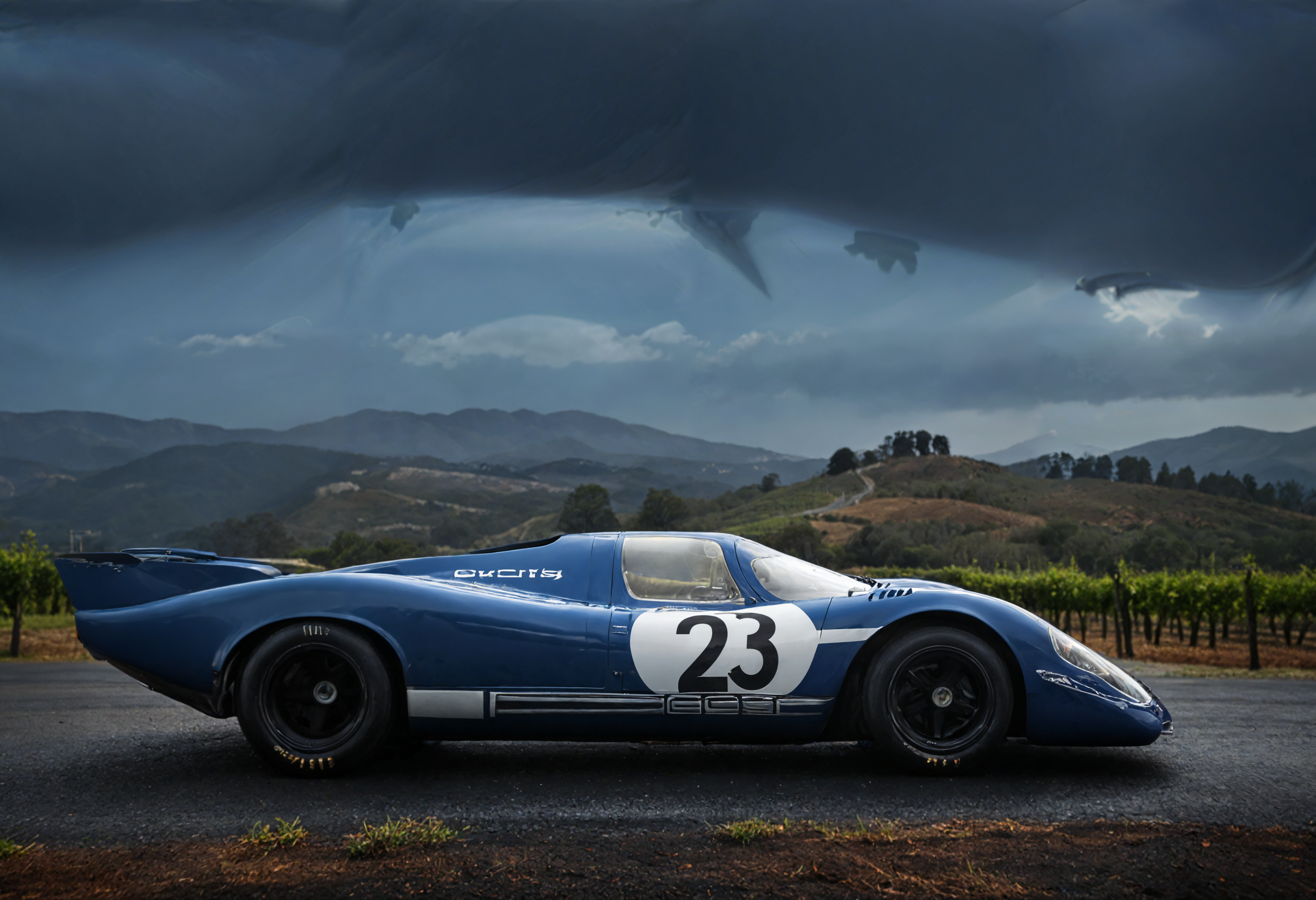 a photograph of a sports car, p0rsche9l7xl,     Overcast Sky: Uniformly covered skies with clouds, diffusing light and creating a moody or somber setting., Indigo Blue,  side view , A moonlit, hilltop vineyard in Napa Valley., dark, low-key,   low color saturation, concept art, perfect composition, masterpiece, professional photography, zeiss lens, shot on dslr 64 megapixels, sharp focus, intricately detailed, dramatic, tilt shift, f/32,