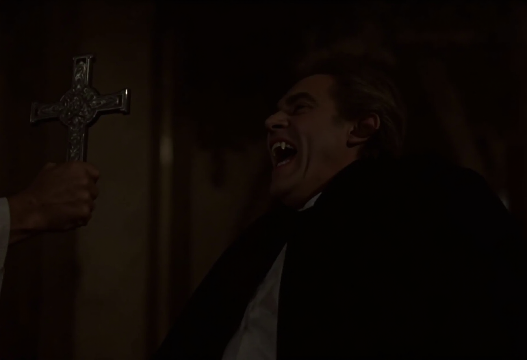 medium shot of a middle-aged aristocratic vampire man recoiling from a priest inside a gothic cathedral. The vampire is standing on the right side of the frame, hissing showing fangs, dramatically billowing his cape. The priest is standing on the left side of the frame, holding a sivler cross towards the vampire directly looking at him. soft warm light at night <lora:hammer-000073:1>