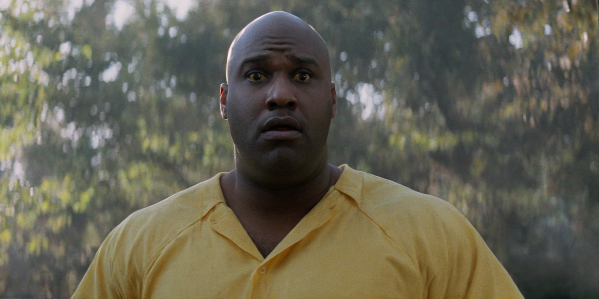 Horror-themed,  <lora:Fright Night 1985 Film Style:1>
Cinematic Medium Shot Film Footage captured by Panavision Cameras and Lenses, a Bouncer a big black bald man in a yellow shirt is holding his hands together with a surprise look on his face, Fright Night 1985 Film Style, Eerie, unsettling, dark, spooky, suspenseful, grim, highly detailed