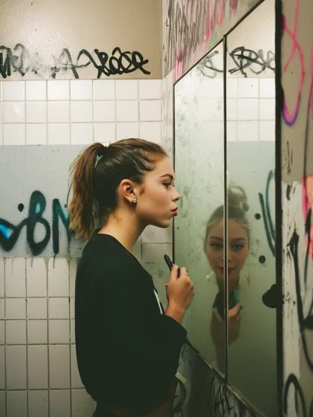 Analog photo of Nellie_LaPlace_P_MXAI_SDXL looking into the mirror in a public bathroom, graffitti on the walls