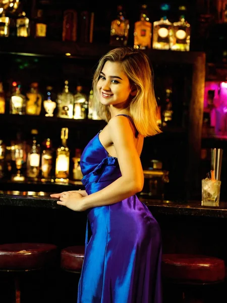 Cinematic fashion photograph Rebekka_Larsson_P_MXAI_SDXL wearing aan elegant silk coctail dress, flirty smile, in an elegant dimly lit cocktail bar, shot from the side Rebekka_Larsson_P_MXAI_SDXL