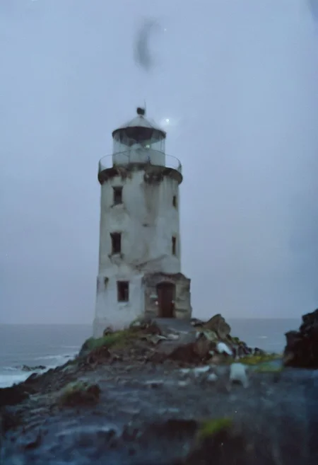 c41_hasselblad_portra400, In a grainy, handheld video, a lone explorer investigates an old, decrepit lighthouse on a foggy night. As he ascends the spiral staircase, strange whispers and ghostly moans fill the air. At the top, he encounters a monstrous, ethereal being with tentacles and multiple glowing eyes. The footage is chaotic and filled with static, capturing the explorer's terror and the creature's unearthly presence.