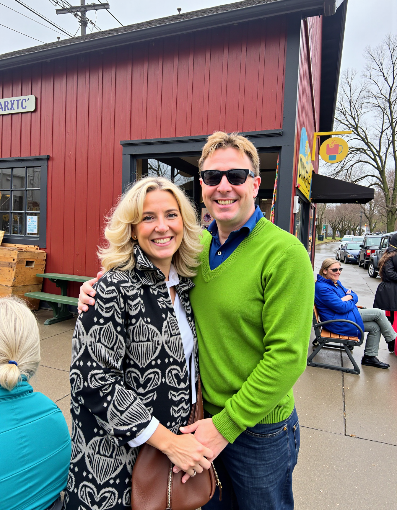 Medium shot photo of a cheerful couple standing close together in an outdoor setting, showcasing a warm and candid moment. The man, with fair skin, a round face, and short blonde hair, is wearing dark sunglasses and a green sweater over a blue collared shirt. He has a wide, joyful smile, and his left arm is wrapped around the woman, adding to the affectionate pose. The woman, with light skin and shoulder-length wavy blonde hair, is smiling broadly as she leans into the man's embrace. She is wearing a black and white patterned coat and carries a brown handbag over her shoulder. In the background, a quaint small-town setting is visible, featuring a red wooden building with a visible sign reading "DUARTE'S," as well as parked cars and power lines. A woman with white hair, dressed in a bright blue jacket, sits on a bench by the building, adding a casual, lived-in aspect to the scene. The lighting is natural, indicating a bright but slightly overcast day, which gives the image a relaxed, everyday quality. The overall mood is friendly and affectionate, capturing a spontaneous moment of connection amid a typical town backdrop <lora:amateurphoto-v5-14-15-1-1:0.45>