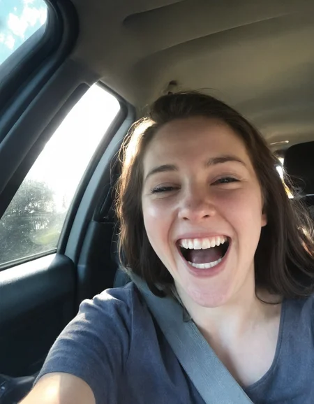Authentic share, Spontaneous, authentic, natural light: Car selfie. Person in driver's seat, light coming through windshield. Seatbelt visible, dashboard and steering wheel in frame. Subject possibly caught mid-laugh or making a face.