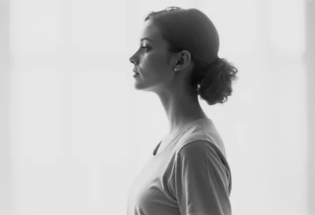 an aesthetic, minimalist depiction of a female profile in side view. she wears a t-shirt. The focus is on the soft contours and calm, monochromatic tones. The scene feels mystical and dreamy, almost as if viewed through a delicate mist, with gentle light accentuating the silhouette. The background is diffuse and creamy white, drawing attention to the elegant simplicity of the figure.