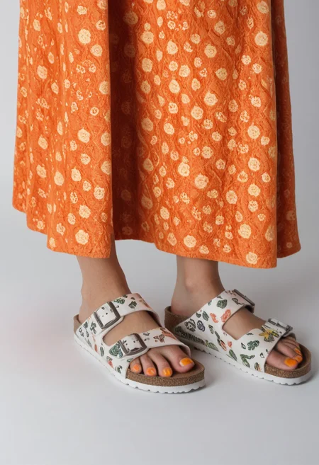1girl, solo, simple_background, white_background, birksonfeet, orange_toenail_polish, close-up, lower_body, footwear_focus, patterned, long_skirt