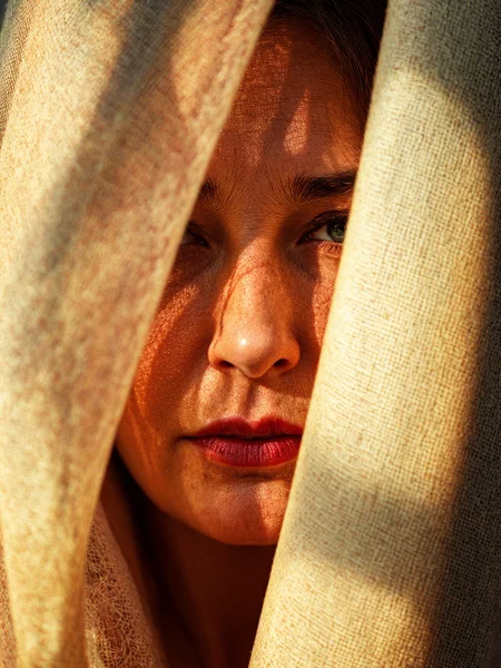 macro photo, textured linen, multicolored, sunlight and shadows, partially covering a (mature) woman's face, in her 40s, mouth closed