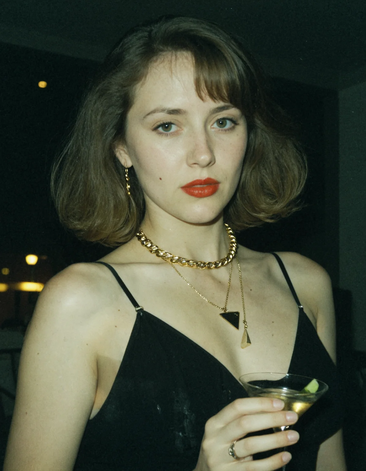photo taken with a compact digital camera from the early 1990s, grainy, washed out colors, flash photography, grainy texture, overexposed light, ethereal mood, low resolution, camera flash, realistic, ultra high quality real image, unreal contrast, low saturation, highlights, photoshoot with camera flash; A beautiful woman, wearing a black dress, a gold necklace around her neck, red lips, holding a martini in her hand.
