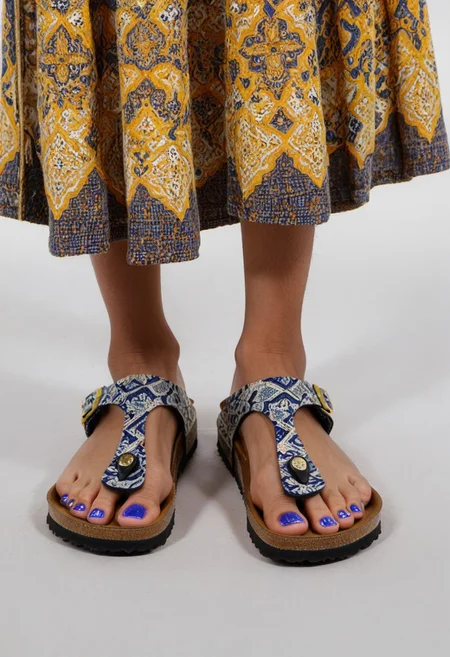 photograph of woman's feet wearing sandals, 1girl, solo, dynamic_pose, simple_background, white_background, gizehonfeet, (yellow and blue toenail_polish), (close-up:0.5), lower_body, footwear_focus, patterned long_skirt