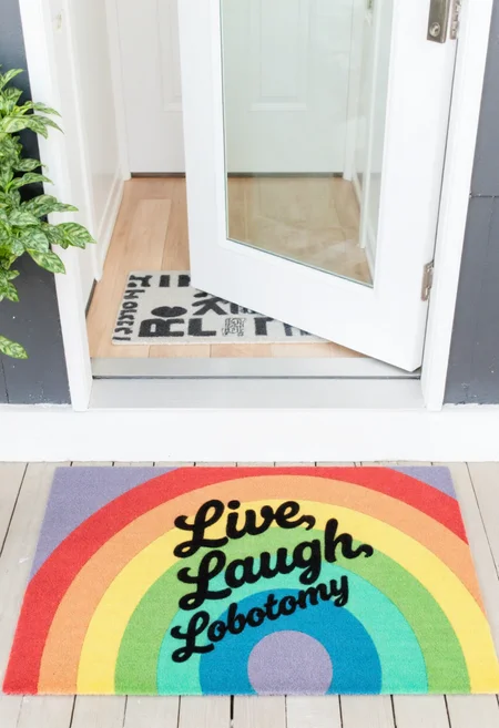 <lora:Welcome_Mat_Manufacturer_FLUX-000023:0.9>
This photograph captures a colorful welcome mat placed in front of a white front door. The mat features a vibrant, colorful design with the phrase "Live, Laugh, Lobotomy" in bold, white, cursive letters.