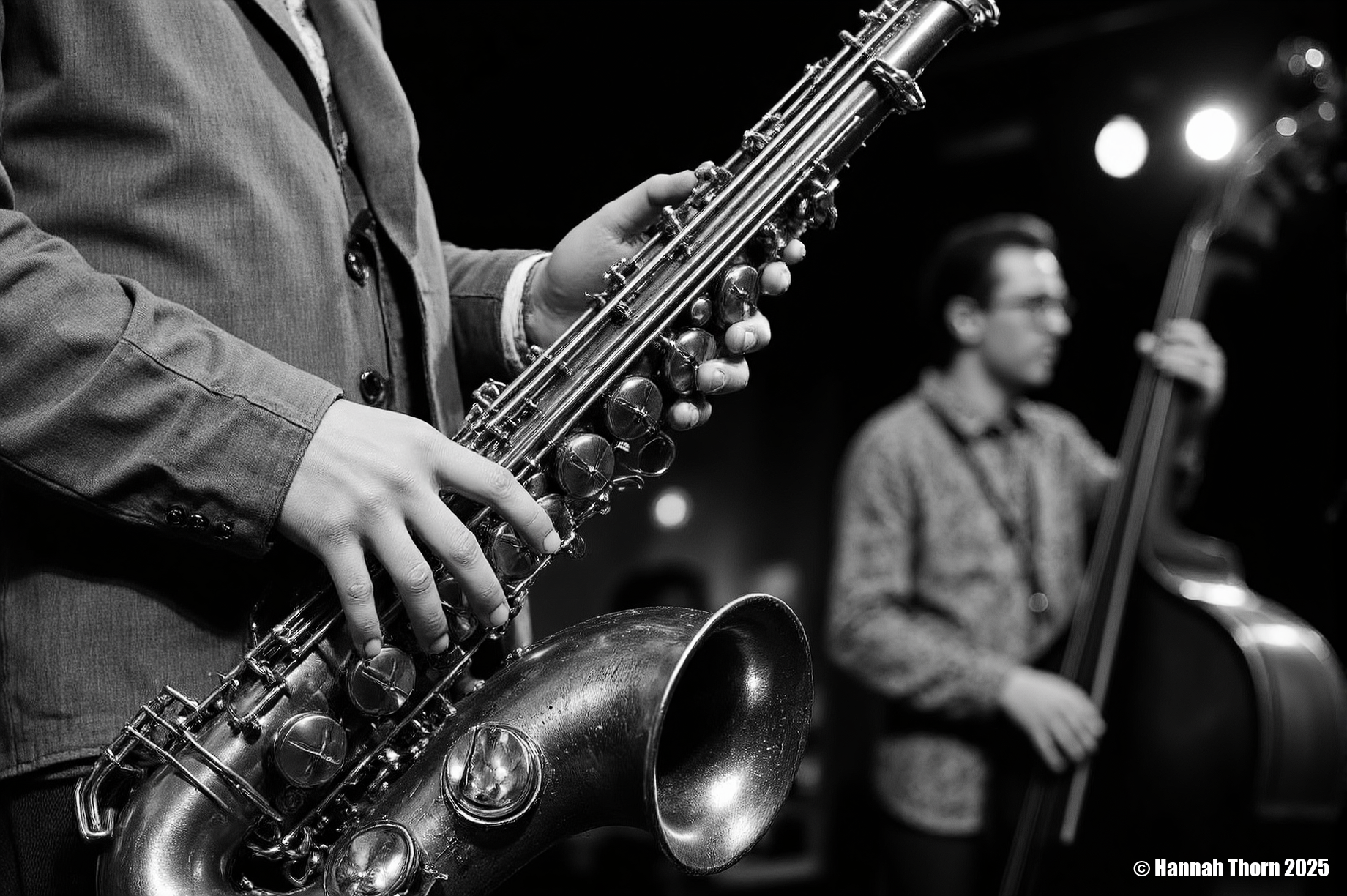 The image is a black and white close-up shot of a saxophonist playing a tenor saxophone.  The focus is sharply on the saxophone and the musician's hands, which are positioned on the instrument's keys and valves.  The saxophone itself appears aged, with a slightly worn look to its metallic surface. The details of the instrument, such as its keys and bell, are clearly visible.  The saxophonist is wearing a somewhat loose-fitting jacket and a visible portion of a collared shirt underneath. The background is significantly out of focus, but shows a blurry figure, seemingly another musician playing an upright bass, suggesting a jazz or blues performance setting.  The background lighting is dim, with some blurred light sources visible, contributing to the moody atmosphere.  The style of the photograph is distinctly **black and white photojournalism** or **concert photography**.  The high contrast, shallow depth of field (emphasizing the saxophone while blurring the background), and the candid feel (as if capturing a moment during a live performance) are all typical of these styles. The monochrome palette enhances the dramatic effect and focuses attention on the texture and form of the saxophone and the musicianâs interaction with it. The overall mood is intimate and intense, conveying the emotion and energy of a live music performance. <lora:_Flux\Vintage_Jazz-Club.safetensors:1.0:1.0>
