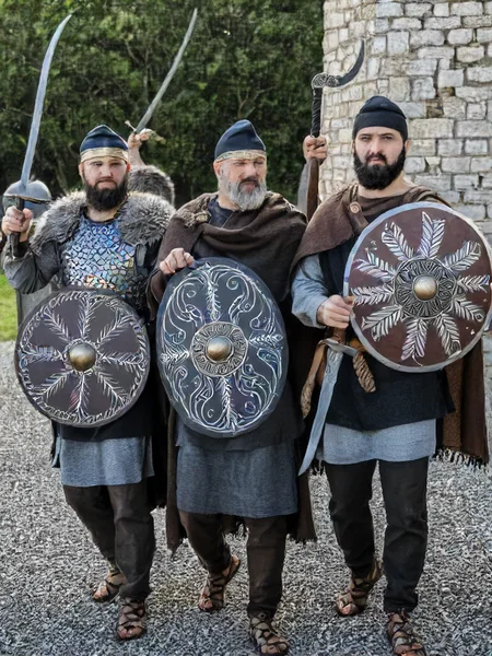 dacian warrior, phrygian cap, falx (weapon), dacian shield, black hair, hat, holding, weapon, male focus, multiple boys, sword, armor, copyright name, facial hair, 3boys, knife, beard, shield, dagger, chainmail, masterpiece photography,8k <lora:dacii:1>