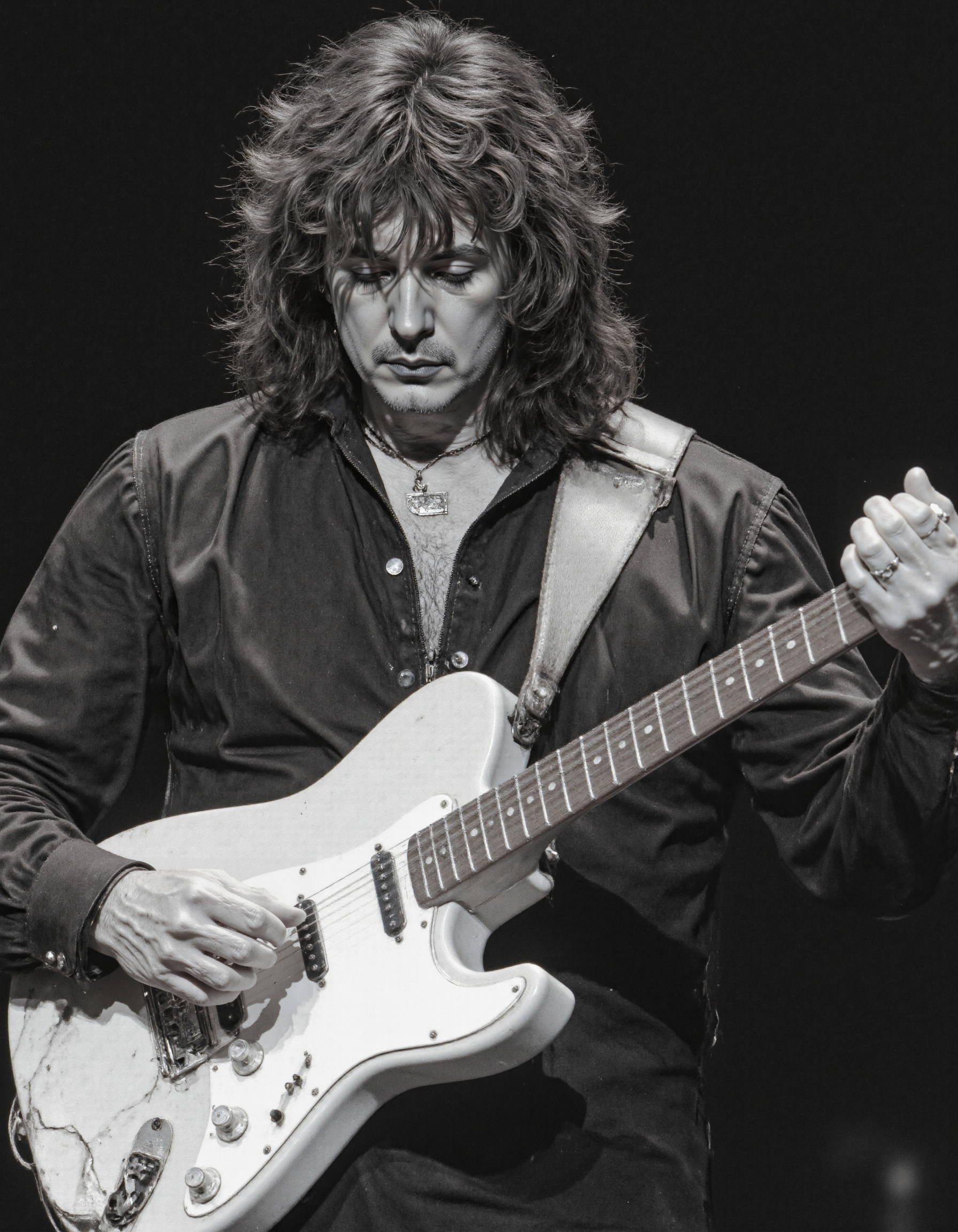 <lora:RICHIE_BLACMORE:1>, This is a black-and-white photograph capturing a man with long, wavy, unkempt hair, possibly in his mid-30s to mid-40s, holding an acoustic guitar. He has a serious expression on his face, looking directly at the camera. The man is wearing a dark, leather jacket that appears worn and textured, with a slight sheen to it. He has a simple necklace around his neck. The guitar he is holding is a six-string acoustic guitar with a natural wood finish. The guitar neck is visible, with the strings extending towards the camera. The background is out of focus, providing a stark contrast to the subject and the guitar, which are sharply in focus. The image has a vintage feel, possibly from the 1970s or 1980s, judging by the clothing style and the overall look of the photograph. The lighting is natural, suggesting an outdoor or indoor setting with natural light. The photograph is a candid moment, capturing a musician in a relaxed and focused state, likely during a performance or rehearsal. The texture of the leather jacket and the roughness of the man's hair add to the raw, authentic feel of the image.