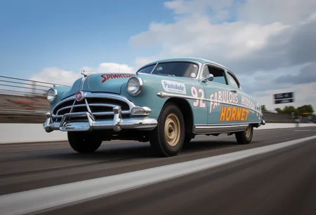 This is the Hudson Hornet, an American passenger car manufactured in 1951.Three-quarter view.low angle.racing around the circuit.The moment it crosses the finish line.finish line is blur..<lora:hudson-hornet:0.8>,