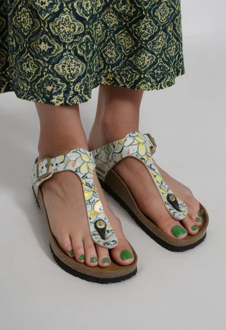 photograph of woman's feet wearing sandals, 1girl, solo, dynamic_pose, simple_background, white_background, gizehonfeet, (green toenail_polish), (close-up:0.5), lower_body, footwear_focus, patterned long_skirt