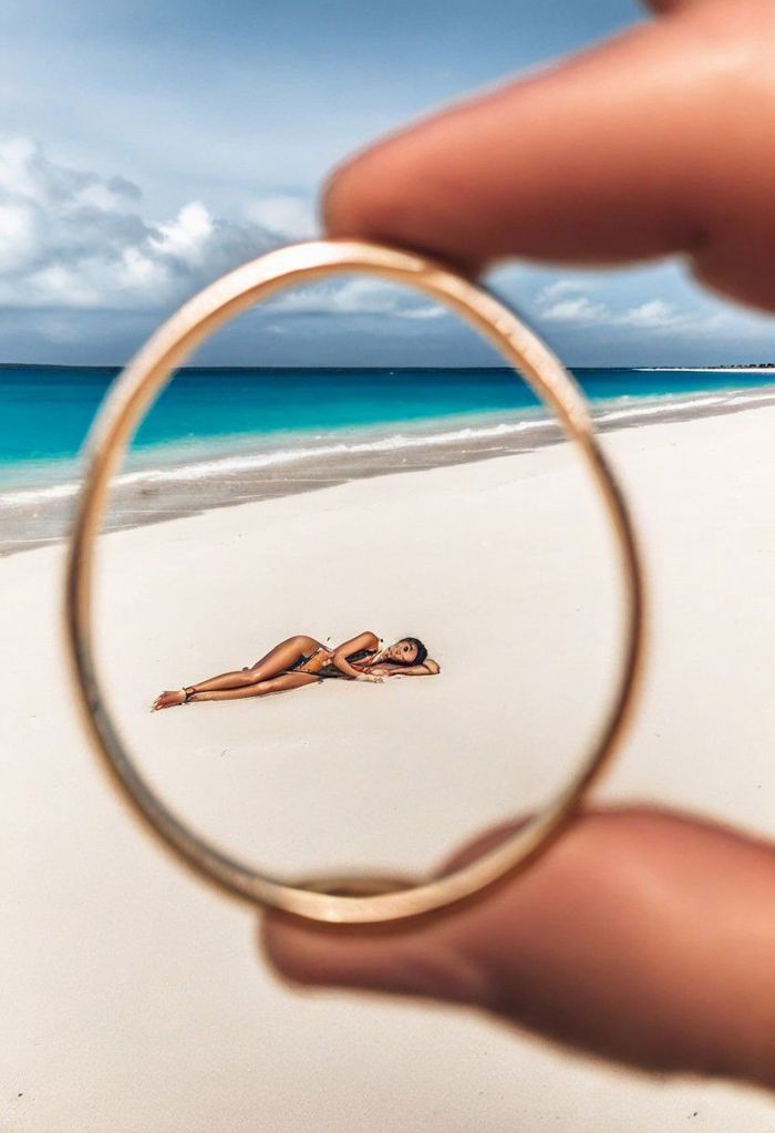 F-B-C, POV, blurry foreground: fingers holding a ring, sharp background: a woman lying on the beach  , effect: the woman is inside the ring