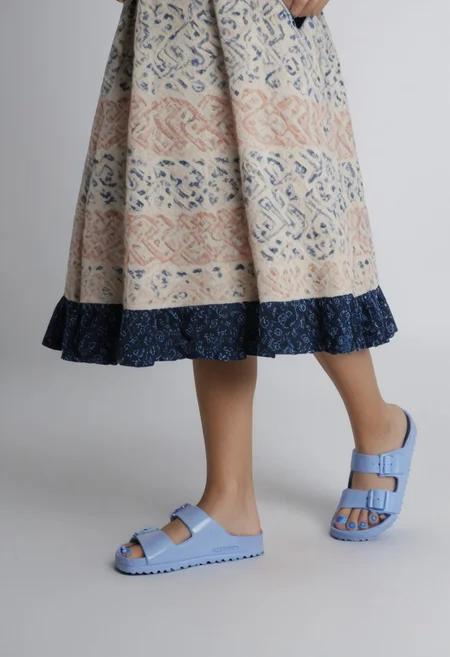 1girl, solo, dynamic_pose, simple_background, white_background, birksonfeet, blue_toenail_polish, close-up, lower_body, footwear_focus, patterned, long_skirt