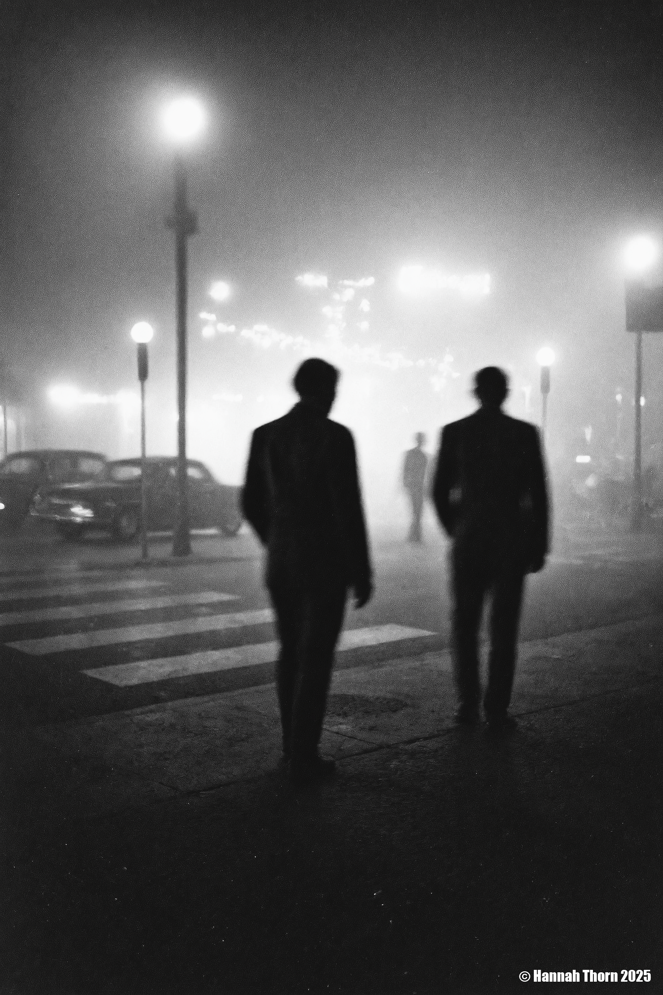 A black and white photograph from a distance camera angle, capturing a foggy night scene with two silhouettes of people in the foreground. the image is taken from a low angle, focusing on the two figures in the middle of the frame, with the fog creating a mysterious atmosphere. on the left side of the image, a man appears to be walking away from the viewer, while on the right side, another figure is blurred, creating a sense of depth and dimension. the man is wearing a long coat, and his face is not visible due to the long exposure. the scene is set in an urban environment, with a cityscape visible through the foggy atmosphere, featuring street lamps casting a warm glow on the city lights in the background. the overall mood is somber and contemplative, as if the two men are lost in thought.<lora:_Flux\Saul_Leiter_BW.safetensors:1.0:1.0>