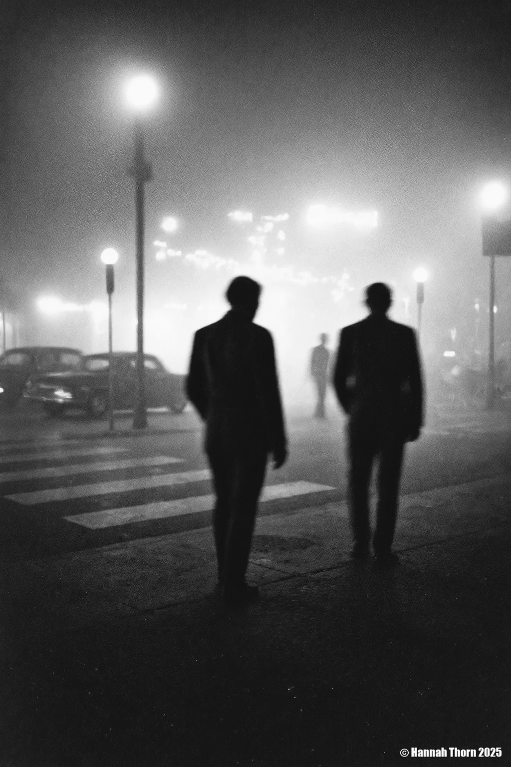 A black and white photograph from a distance camera angle, capturing a foggy night scene with two silhouettes of people in the foreground. the image is taken from a low angle, focusing on the two figures in the middle of the frame, with the fog creating a mysterious atmosphere. on the left side of the image, a man appears to be walking away from the viewer, while on the right side, another figure is blurred, creating a sense of depth and dimension. the man is wearing a long coat, and his face is not visible due to the long exposure. the scene is set in an urban environment, with a cityscape visible through the foggy atmosphere, featuring street lamps casting a warm glow on the city lights in the background. the overall mood is somber and contemplative, as if the two men are lost in thought.<lora:_Flux\Saul_Leiter_BW.safetensors:1.0:1.0>