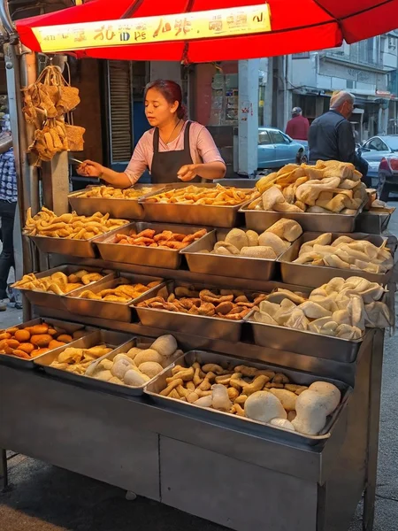 A street food stall manned by an attractive Asian woman, set up along a bustling sidewalk. She is actively preparing or serving food, her appearance reflecting both professionalism and beauty. The colorful and inviting stall displays a variety of local delicacies. Steam or smoke rises from the cooking equipment, adding to the ambiance. The background captures the lively street scene with pedestrians showing interest in the food. The scene should be as realistic as a high-resolution photograph, with natural lighting that highlights the vibrant colors and textures of the food, the authenticity of the street setting, and the allure of the vendor,   <lora:t9m:0.75>