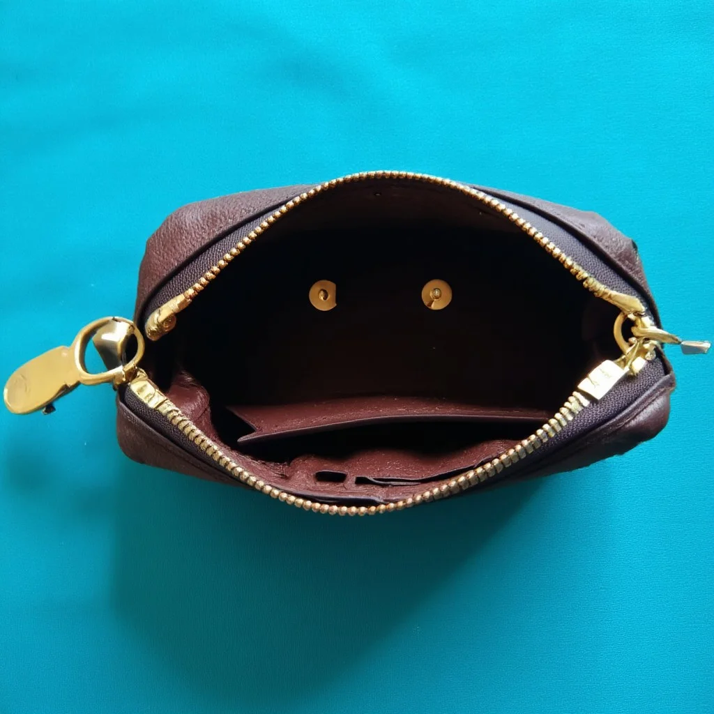 A pareidolia image of a sad face made by an empty open coin purse laying on a cyan cloth table. 
The coin purse has golden clutches and brown leather.
The dominant colours of the image are deep rich cyan and gold.
