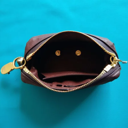 A pareidolia image of a sad face made by an empty open coin purse laying on a cyan cloth table.
The coin purse has golden clutches and brown leather.
The dominant colours of the image are deep rich cyan and gold.