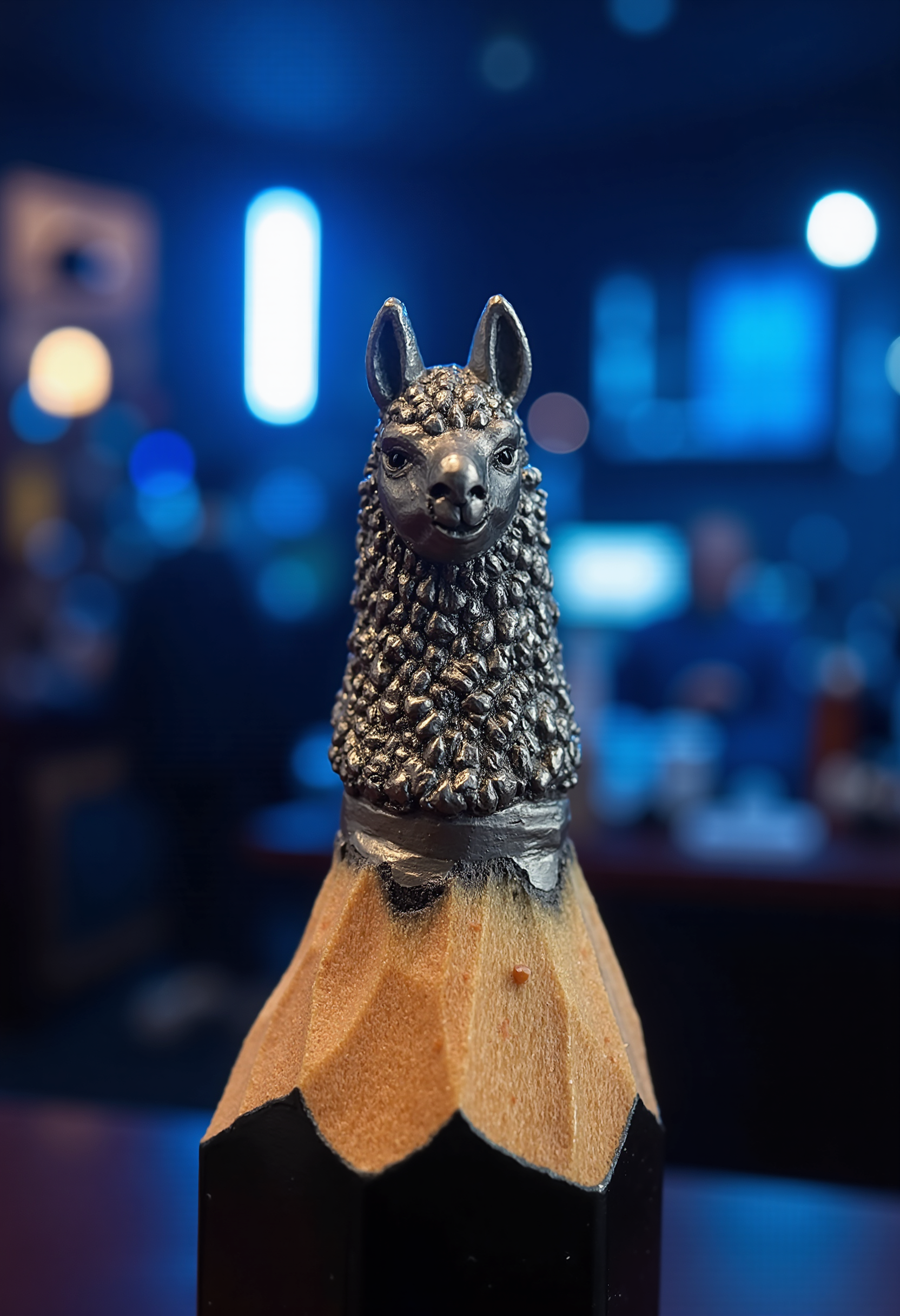 Mini sculpture on the tip of the pencil, showing a llama head potrait. The background is a night bar with blue lights.  