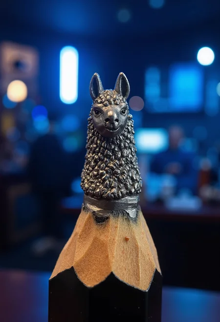 Mini sculpture on the tip of the pencil, showing a llama head potrait. The background is a night bar with blue lights.