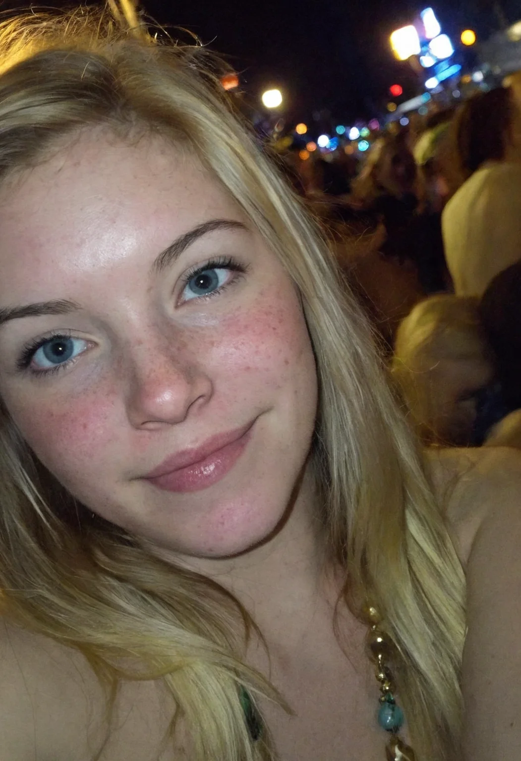 Amateur cellphone photography capturing a cute and attractive young woman with blonde hair at Mardi Gras during a stunning sunset. The scene is vibrant with the festive atmosphere of the parade, colorful beads, and lively crowds in the background. The woman has a playful smirk on her face, exuding confidence and charm, with subtle freckles (freckles:0.2) adding a touch of natural beauty. The photo is taken with a Samsung Galaxy in challenging lighting conditions—poor lighting, low light, and underexposed—resulting in a high-contrast image with deep shadows and bright highlights. The composition emphasizes the woman as the focal point, with the warm hues of the sunset casting a golden glow on her features, while the surrounding environment remains moody and atmospheric. The imperfections in the photo, such as graininess and slight blur, add to the raw, authentic feel of amateur photography.