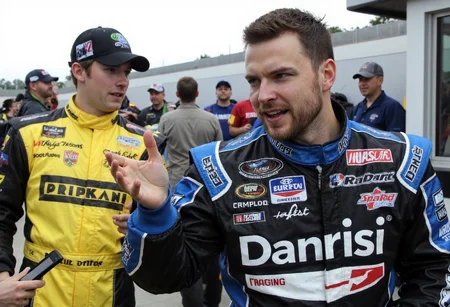 s2ms8ng . Nascar racecar driver wearing a jumpsuit with lots of diffrent sponsor logos. large text on jumpsuit that says "Danrisi racing" . getting interviewed next to racetrack <lora:Samsung_UltraReal:1.0000000000000002>