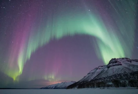 The Aurora Borealis, also known as the Northern Lights, is a mesmerizing natural wonder that illuminates the night sky in a symphony of colors. A dynamic dance of green, blue, and pink hues, it creates an ethereal atmosphere that takes one's breath away. Swirling and shimmering like an otherworldly veil, this celestial spectacle seems to pulse and undulate, as if guided by some mystical force. It is a sight so captivating that one could stand in awe for hours on end, lost in its transcendent beauty. The Aurora Borealis is truly a masterpiece of nature, an enchanting spectacle that leaves all who witness it in wonder and amazement.
