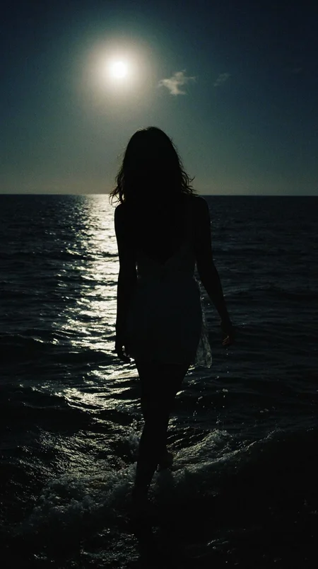 8n8log, Silhouette of a woman, walking into the ocean, illuminated by moonlight, mid-20s, long wavy hair cascading down her back, elegant posture, no visible clothing details, water reflecting the bright moon, creating a serene and mystical atmosphere, calm waves, horizon line slightly visible, slightly blurred details, nighttime setting, tranquil composition. film photography aesthetic, film grain effect prominent throughout image, high contrast lighting creating dramatic shadows, grainy film-like texture, professional photography technique, dramatic chiaroscuro lighting effect