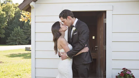 Candid photography of a couple embracing and kissing in front of a charming country chapel. The bride is wearing a stunning white wedding dress with intricate lace details, and the groom is dressed in a classic black tuxedo. They are standing in front of the small, wooden chapel on a sunny day. The bride's arms are wrapped around the groom, and his hands are gently placed on her waist. The soft sunlight illuminates the scene, creating a romantic and joyful atmosphere. The chapel and nature surrounding them add to the peaceful and loving moment. <lora:Sherry-00:1><lora:SelestaFlux1:1>