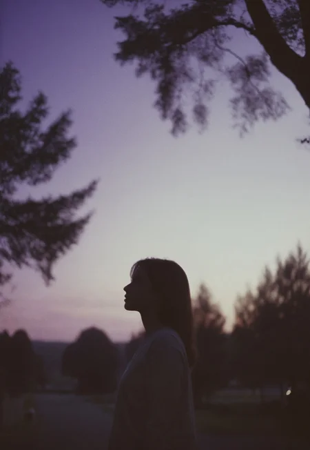Film still, silhouette of a Girl Standing (out of focus) surrounded by trees, Twilight purple sky behind her,, Nikon F3, Nikon AF-NIKKOR 35mm f/2D Lens, kodak vision 3 500t Film, ISO 400, f/2.8, 35mm Film, Film Grain, film halation, Film look, Cinematic, epic cinematic color style
