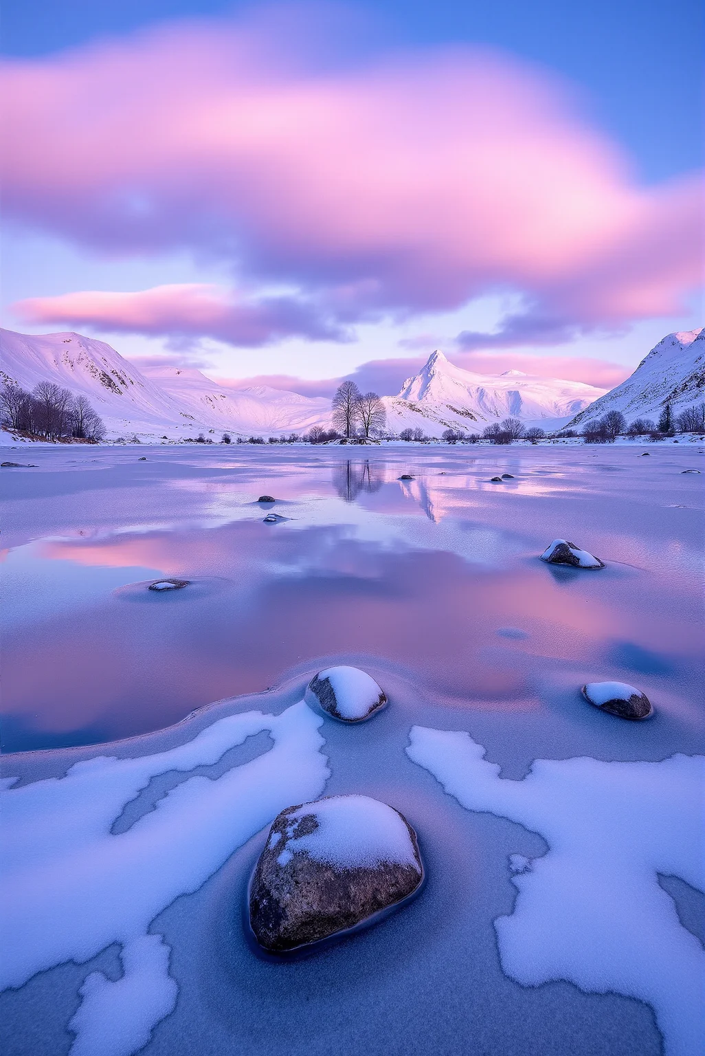 <lora:Ice_Desert_style:0.8> IceDesert style.
A tranquil, frozen lake lies still beneath soft pastel skies, its surface textured with crystallized ice ridges, frozen ripples, and isolated snow patches glistening under the morning light. In the distance, gently rounded mountains wrapped in thick snow blush with warm alpenglow, casting a soft, luminous pink against the surrounding blue dusk. Cotton-candy clouds drift in layered streaks above, their delicate shapes mirroring the undulating mountain ridges. Captured with long exposure in a low-angle frontal composition, the image emphasizes dreamlike atmosphere and the chromatic blending of lavender, rose, and periwinkle. Scattered rocks and leafless trees frozen into the shoreline add tactile contrast, while reflections shimmer faintly in the shallow frost-mottled water. The moment glows with quiet intensity—an intimate balance between crisp cold and the first tender light of a frozen dawn.