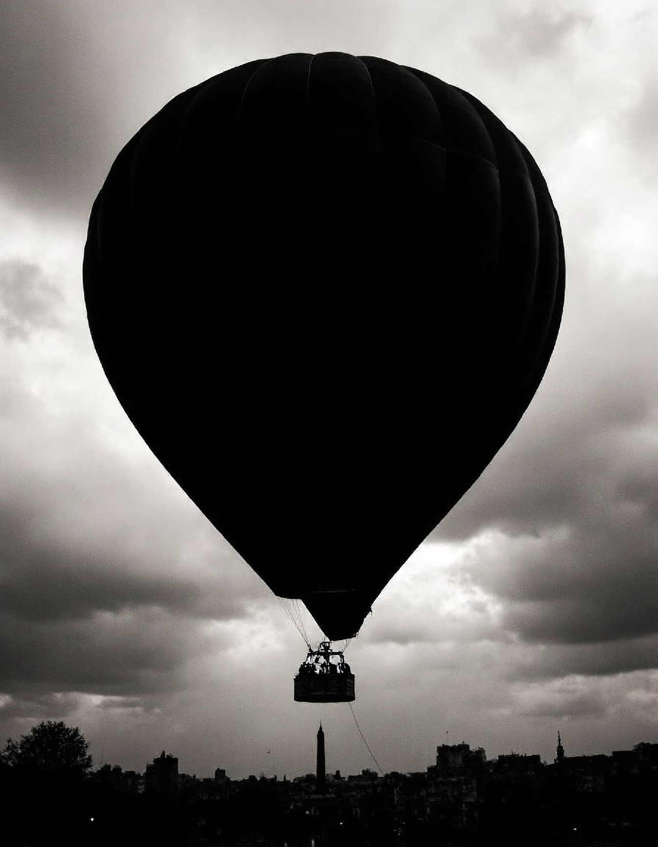 High-contrast black and white photograph, a colossal hot air balloon silhouetted against a stormy Parisian sky, intricate basket details visible, dramatic lighting, shallow depth of field, Canon EOS 5D Mark IV, 85mm lens, f/2.8, ISO 400.