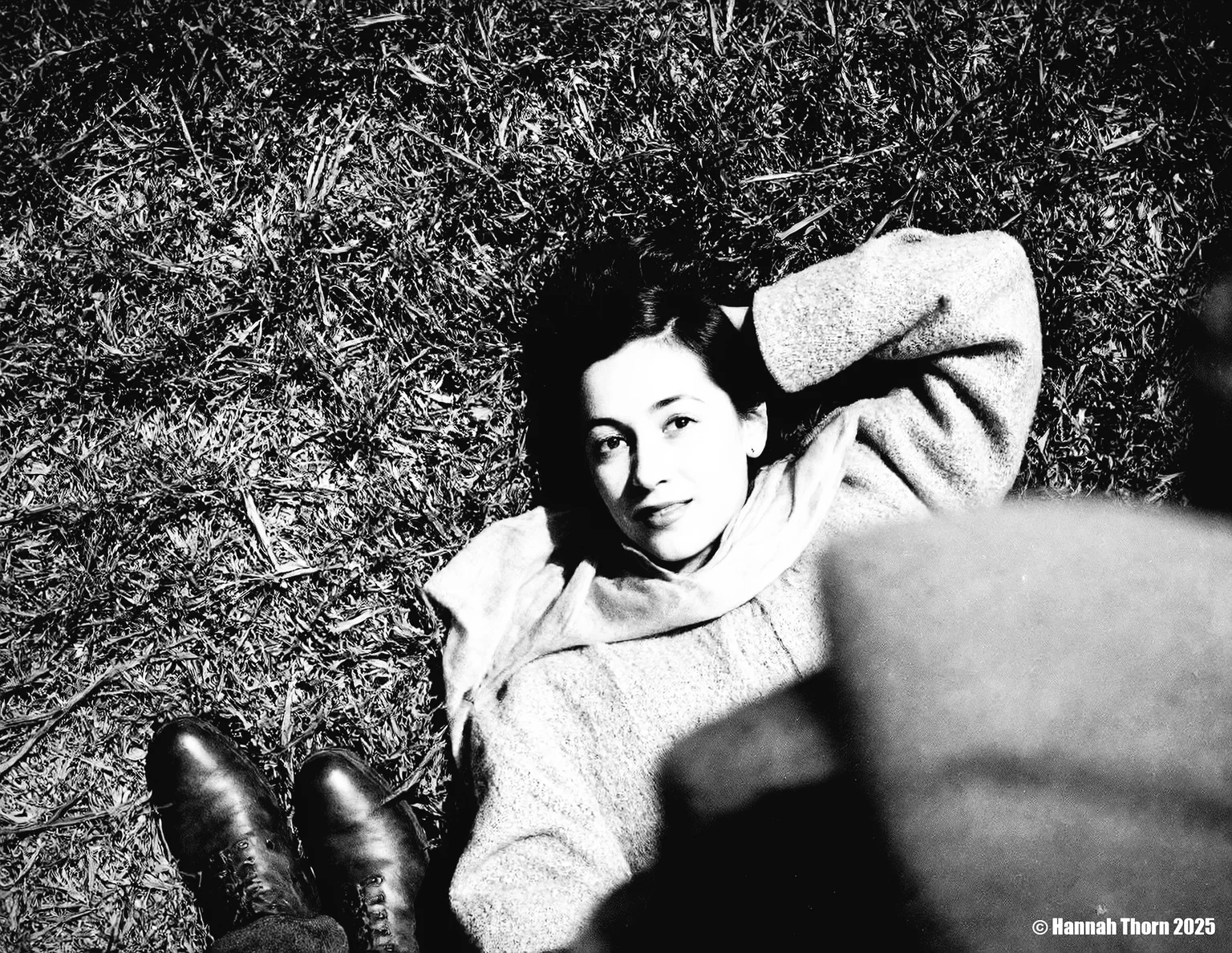 A black and white photo from a bird's eye view about a woman lying on the grass, looking directly at the viewer with a contemplative expression. the subject, a woman with light skin and dark hair, is lying on her back in the center of the image, wearing a knitted sweater and a scarf around her neck. she has a slim body and is positioned in the middle of the frame, with her head resting on her hand. her expression is serene and contemplative, with a hint of a smile on her lips. she is wearing a pair of brown boots on her feet, and her dark hair is styled in a way that frames her face. the background is a patch of grass, and the lighting is soft and natural, casting gentle shadows on her face and body. the overall mood is peaceful and intimate, creating a sense of calmness and tranquility.<lora:_Flux\Saul_Leiter_BW.safetensors:1.0:1.0>