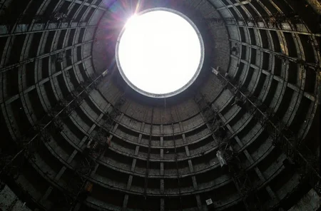 l3n0v0. ultra-wide 16 mm upward shot, inside colossal concrete missile-silo shaft, concentric steel catwalks spiraling toward circular sky aperture, blinding noon sun rim-lighting upper rim, brilliant lens flares from bluish industrial floodlights, crane hook dangling in silhouette against crisp cyan sky, cold matte concrete walls with subtle moisture sheen, deep cobalt shadows, faint orange rust on railings, early-2000s digital-camera bloom and sensor noise, Mirror’s Edge × Half-Life-2 industrial vibe. amateur quality, candid style
