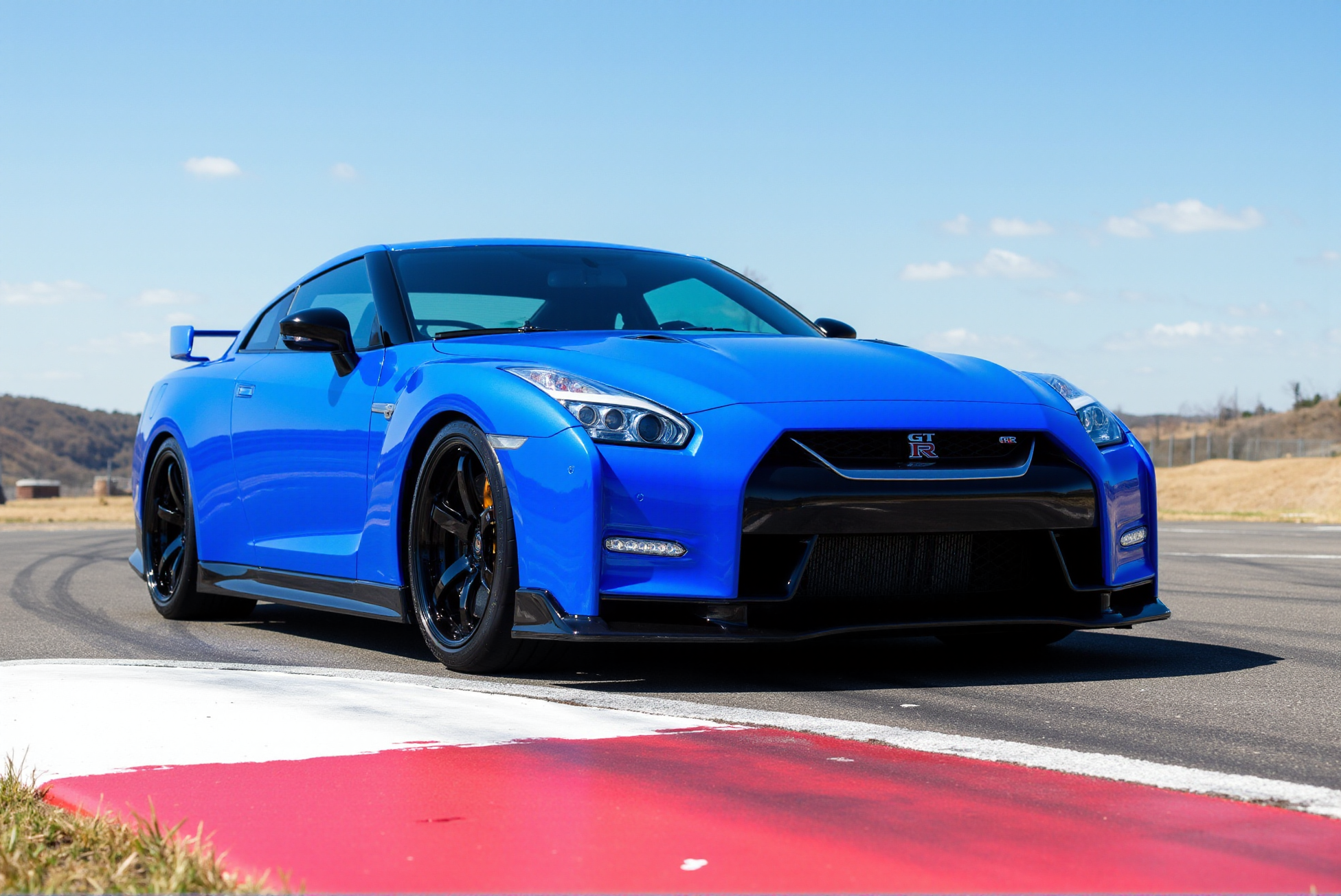 <lora:Nissan_GT-R_R35:0.8> 
A deep metallic blue Nissan GT-R R35 rests calmly under a softly clouded sky, captured in warm golden-hour lighting on a gravel-covered open lot. The low-slung stance, sharply sculpted hood, and flared front wheel arches convey poised aggression, while the sleek aerodynamic body panels reflect the muted amber light. The front grille prominently features the GT-R emblem set just above the chrome Nissan badge, both gleaming with subtle intensity. Multi-spoke alloy wheels finished in brushed silver house ventilated brake rotors and red Brembo calipers stamped with white branding. The side mirrors and front splitter echo dark gloss finishes, and the slight tilt in the camera angle adds a cinematic tension. Faint reflections ripple across the body, and thin wisps of fencing in the distance add scale and openness to the composition. The contrast between the grounded solidity of the vehicle and the expansive background builds visual drama, emphasizing the GT-R R35âs balance of power and elegance. Subtle tire tread texture and shadow gradation beneath the chassis provide depth and tactile realism, enhancing the visual gravity of this iconic performance coupe in a still, contemplative moment.