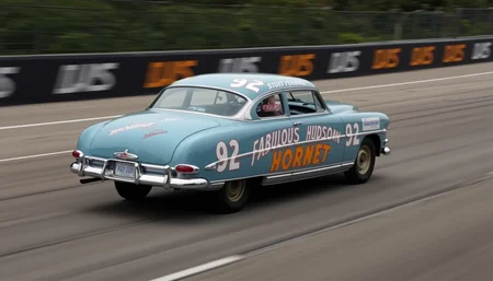 This is the Hudson Hornet, an American passenger car manufactured in 1951.from side.low angle.A panning shot of a car racing around a circuit.. <lora:hudson-hornet:0.8>,