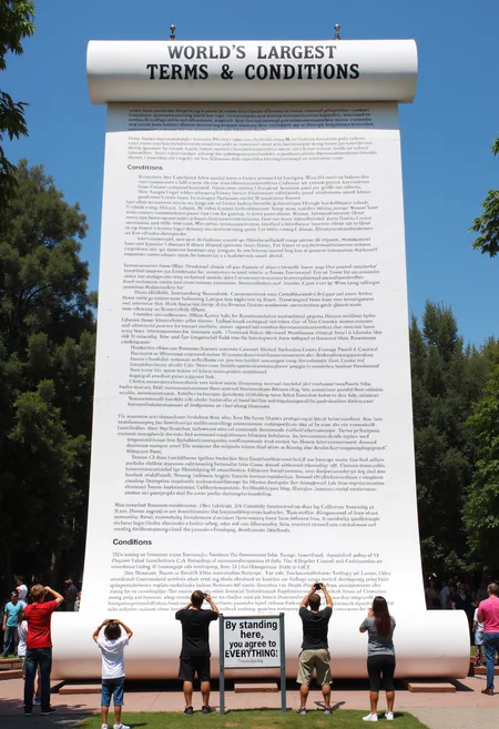 Photo depicting a skyscraper-sized paper scroll of dense legal jargon in a park that is titled, "World’s Largest Terms & Conditions". A sign at the bottom reads: "By standing here, you agree to EVERYTHING." People stand around it taking pictures.