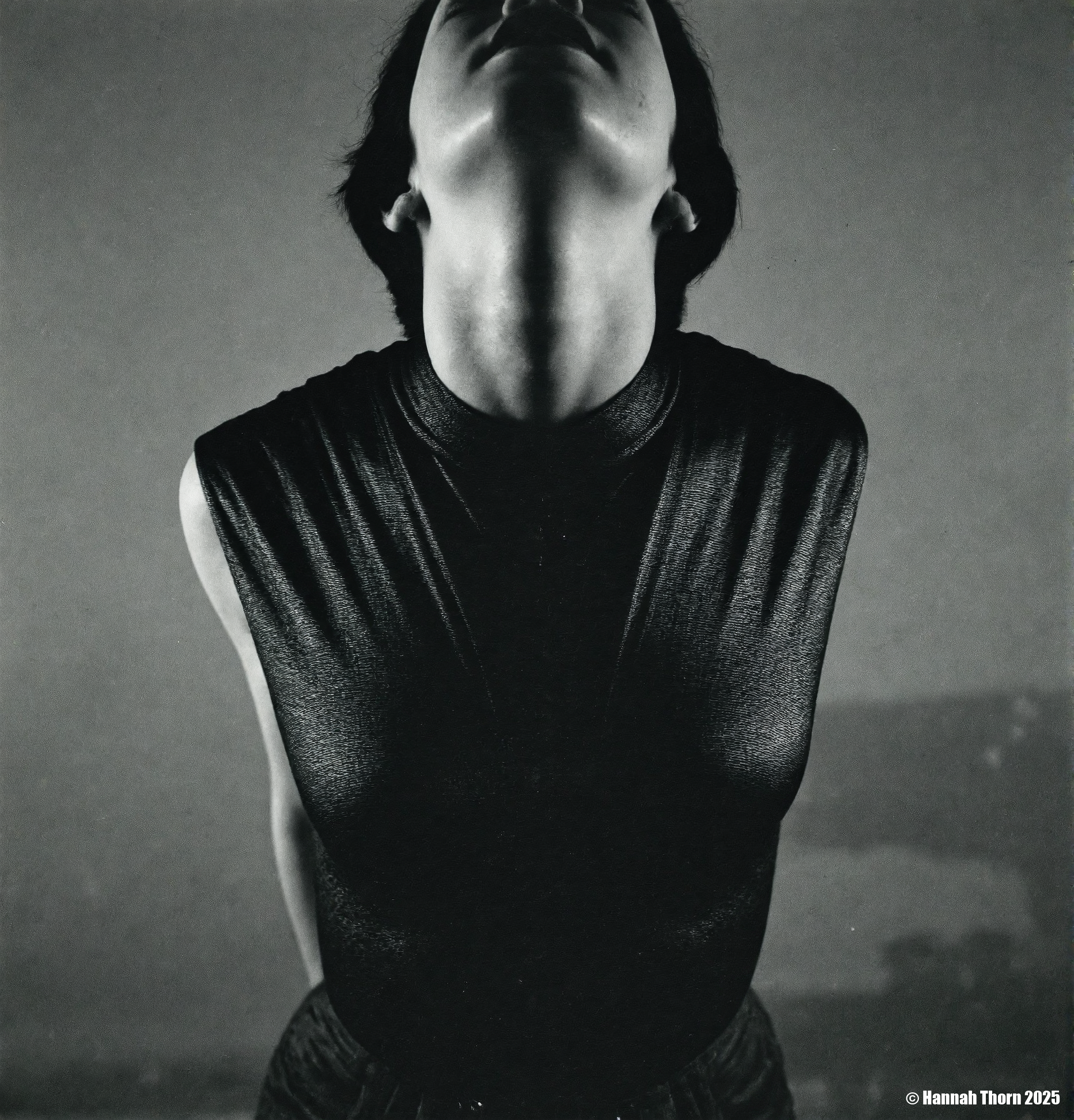 A black and white photo from a frontal camera angle, featuring a  mannequin wearing a sleeveless, textured black top, positioned in the middle of the frame. the woman, who appears to be in her mid-twenties, has short, dark hair and a slim, muscular physique. she is facing the viewer, with her eyes closed and her mouth slightly open, as if she is in a state of contemplation. the background is a plain, muted grey wall, and the lighting is soft and diffused, casting shadows that accentuate the  woman's face and upper body. the overall mood of the image is somber and unsettling, with a focus on the figure's facial features and clothing.<lora:_Flux\Saul_Leiter_BW.safetensors:1.0:1.0>