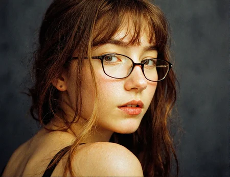 8n8log, extreme close-up portrait of a teen girl, light skin, styled with straight hair cascading down her shoulders, adding playful texture and volume, subtle center-parted bangs framing her face. She is wearing thin, rectangular metal-framed glasses typical of early 2000s fashion, glossy nude lips, lightly flushed cheeks, and thin, arched eyebrows that emphasize her delicate facial features. Her expression is self-assured and composed, with her gaze slightly off-camera. bright soft lighting highlighting her facial features, glasses, and textured hair, capturing the vibrant and stylish essence of early 2000s trends. strands falling across face, slight off-center position to the left of the frame, body slightly turned toward viewer, golden lighting emphasizing facial features, soft glow around eyes and cheekbones, subtle shadows on parts of face, dark-grey out-of-focus background, soft intimate melancholic atmosphere. film photography aesthetic, film grain effect prominent throughout image, 